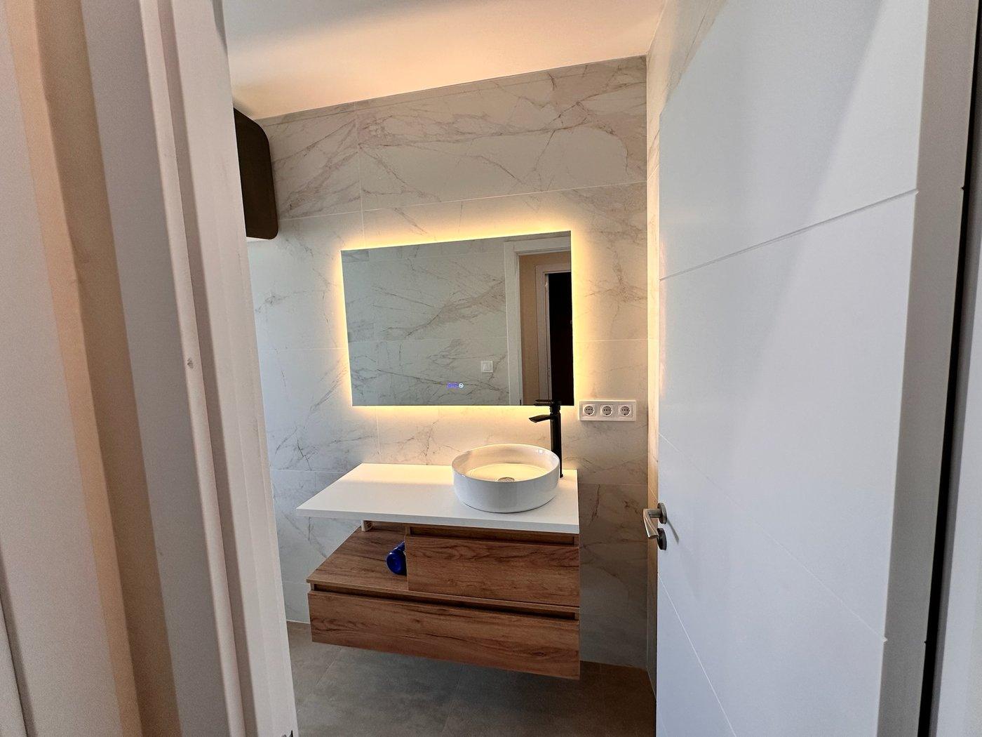 Baño reformado por G-Instal con mueble suspendido en madera y espejo retroiluminado